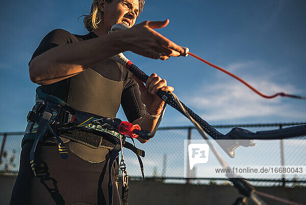 A woman in a wetsuit rigs up her kite on the beach before kiteboarding