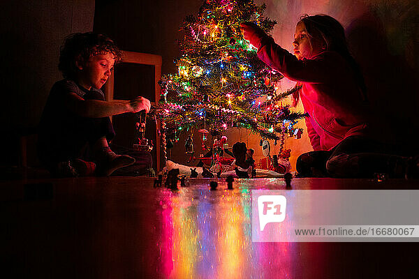 Geschwister schmücken ihren Weihnachtsbaum bei Nacht