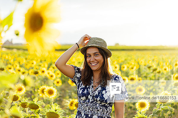 Junge attraktive brünette Frau posiert in ihrem Designerkleid in einem Sonnenblumenfeld und trägt einen Hut