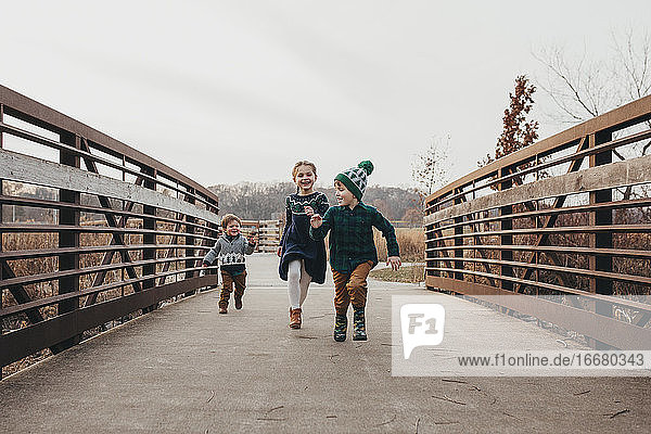 Geschwister laufen gemeinsam auf der Brücke in Richtung Kamera