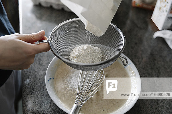 High angle of crop person sieving flour for cooking pastry in kitchen