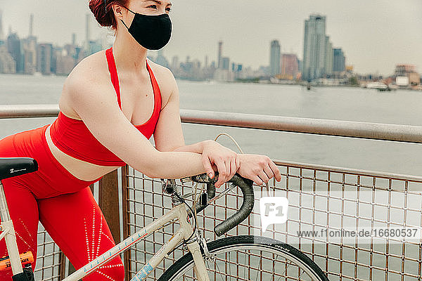 Junge Radfahrerin mit Gesichtsmaske und Fahrrad am Wasser