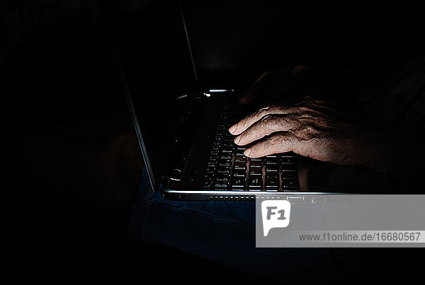Anonyme ältere Person  die in der Dunkelheit einen Laptop benutzt