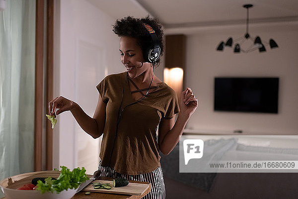 Zufriedene afroamerikanische Frau mit Kopfhörern beim Kochen von Salat