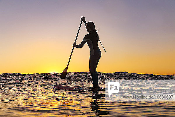 Weiblicher Sup-Surfer bei Sonnenuntergang