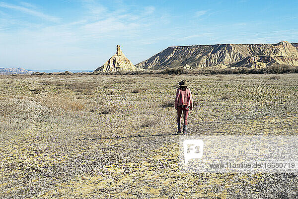 Rückansicht einer Frau in rosafarbener Kleidung  die an einem sonnigen Tag in einer Wüste spazieren geht