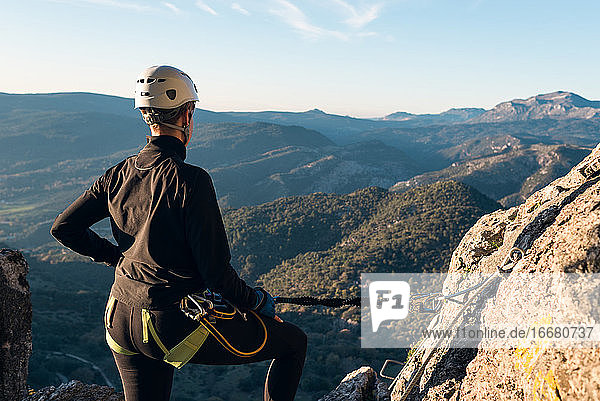 Konzept: Abenteuer. Bergsteigerin mit Helm und Klettergurt. Blick von hinten auf die Naturlandschaft von Andalusien. Mit einem Karabinerhaken an der Naturwand gesichert. Klettersteig in der Bergwelt