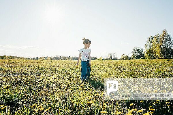 Mädchen geht mit Blumen in der Hand durch ein gelbes Blumenfeld