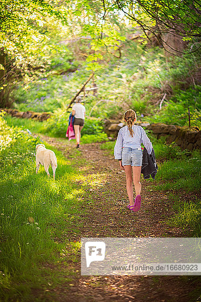 Mädchen geht mit Mutter und Hund einen Waldweg hinauf