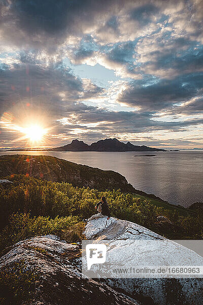 Mann sitzt auf einem Felsen und schaut auf eine Berginsel bei Sonnenuntergang
