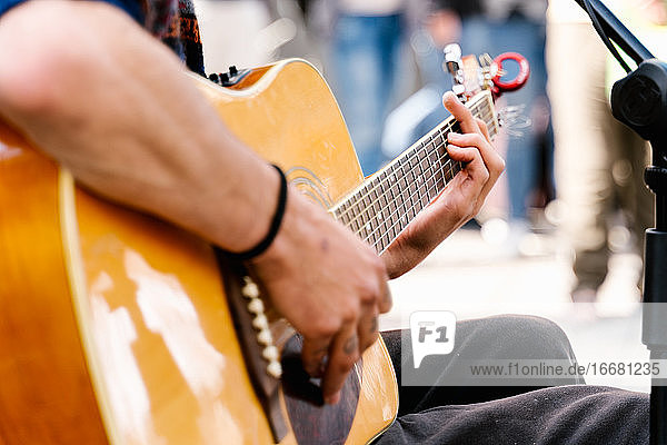 Selektiver Fokus auf die Hände eines jungen Mannes  der auf einer belebten Straße Gitarre spielt