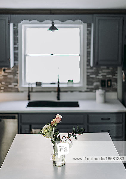 weiße Küchenarbeitsplatte mit Blumen und Vase und Fenster im Hintergrund