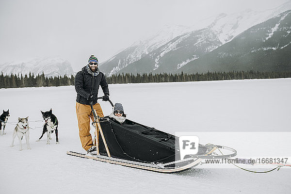 Mann und Frau sitzen und stehen im Hundeschlitten in den kanadischen Rocky Mountains