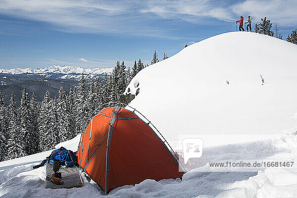 Male and female hiker standing on snowcapped mountain while tent in foreground