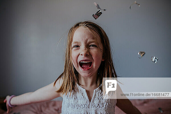 Porträt eines jungen Mädchens  das fröhlich silbernes Konfetti wirft