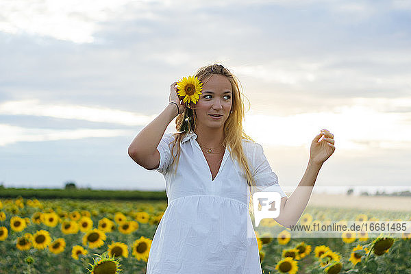 Young attractive blonde woman posing in her designer dress in a field of sunflowers