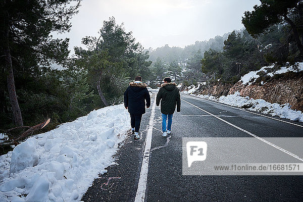 Zwei Freunde gehen eine schneebedeckte Straße entlang