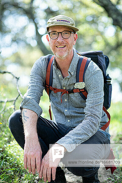 Portrait of backpacker kneeling on trail and smiling in California