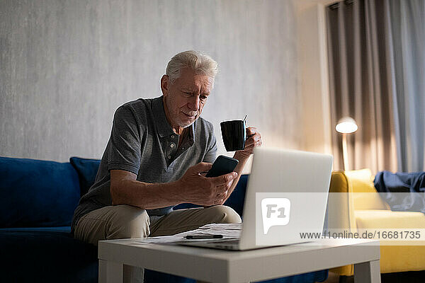 Älterer Mann mit Tasse und Smartphone