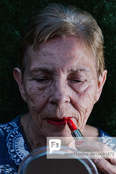 Alte Frau malt ihre Lippen rot an und betrachtet sich im Spiegel