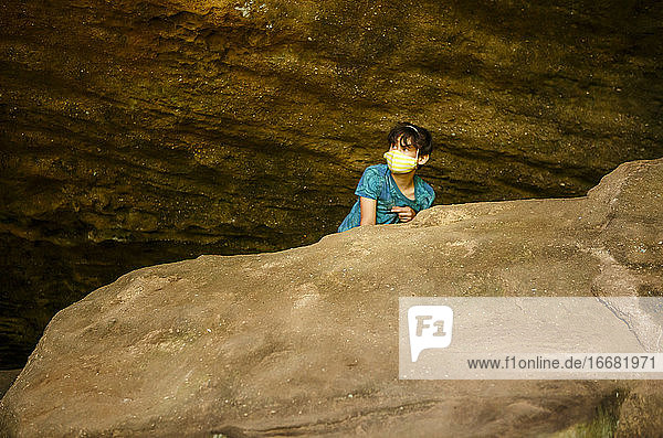 Ein Junge mit Gesichtsmaske späht über einen großen Felsen in einer Sandsteinschlucht