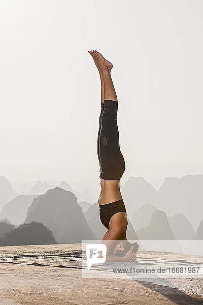 schöne Frau  die oberhalb der kastigen Berge von Yangshuo Yoga praktiziert