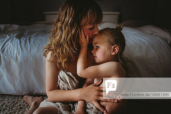 Mutter  die ihre Tochter küsst  während sie sich im Schlafzimmer Haut an Haut umarmt