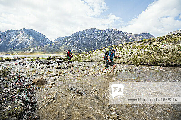 Two backpackers crossing flooding river in Akshayak Pass