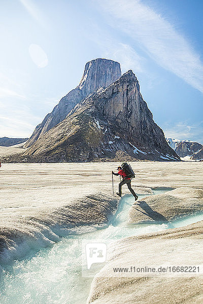 Backpacker hikes over glacial river below Mount Asgard  Baffin Island.
