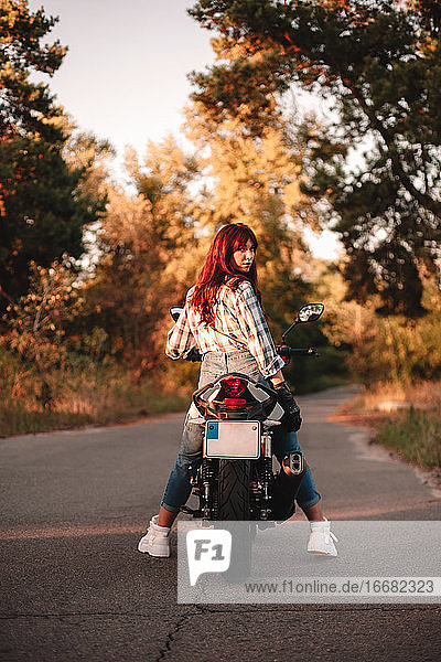 Selbstbewusste Frau  die auf einem Motorrad sitzend über die Schulter in die Kamera schaut