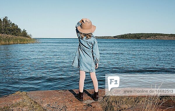 junges Mädchen  das seinen Hut festhält und auf das finnische Meer hinausschaut