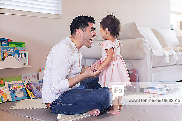 Vater sitzt auf dem Boden im Wohnzimmer und lächelt seine kleine Tochter an