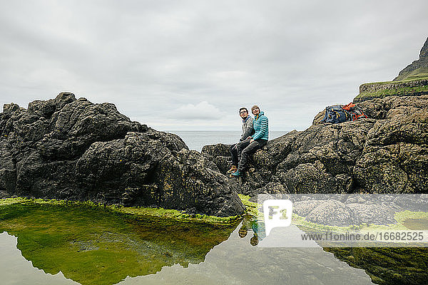 Paar sitzt auf Steinen in der Nähe von ruhigem Meerwasser