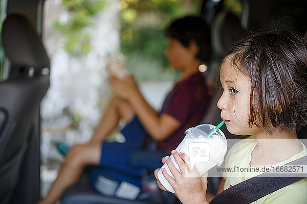 Zwei Kinder sitzen im Sommer im offenen Auto und nippen an kalten Getränken