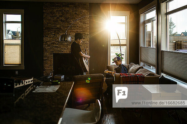 Brothers playing guitar at home with sun coming in window