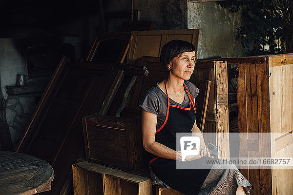Nachdenkliche Frau sitzt in einer Werkstatt  umgeben von alten Holzgegenständen