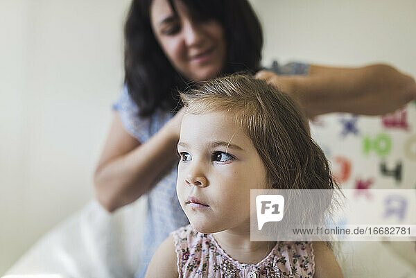 4 Jahre altes Mädchen mit großen braunen Augen und lächelnder Mutter  die ihr Haar flechtet