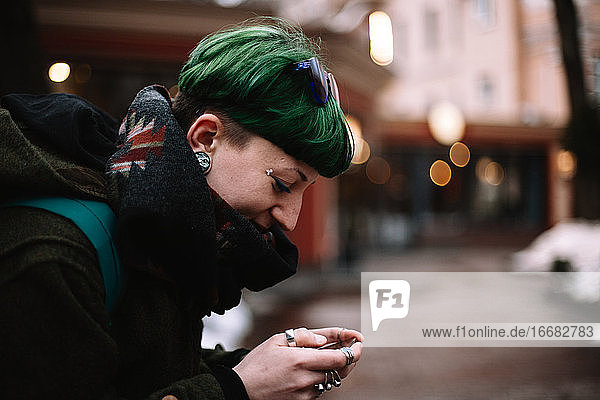 Porträt einer glücklichen nicht-binären Hipster-Frau  die ein Smartphone in der Stadt benutzt