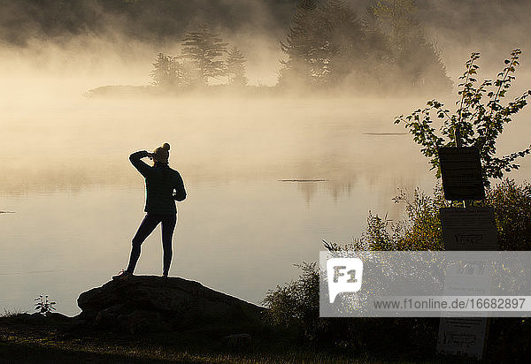 Junge Frau blickt auf den Sonnenaufgang am nebelverhangenen Vermont-See
