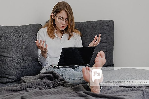 Attractive Young Woman Working from Home - Female Entrepreneur Sitting on sofa with Laptop Computer and Checking Cell Phone from Comfort of Home