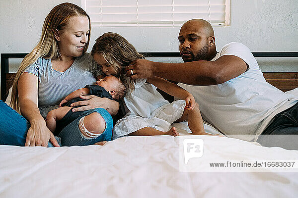 Gemischtrassige Familie kuschelt im Bett mit neugeborenem Baby