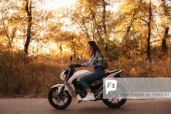 Junge selbstbewusste Frau fährt Motorrad auf Landstraße bei Sonnenuntergang