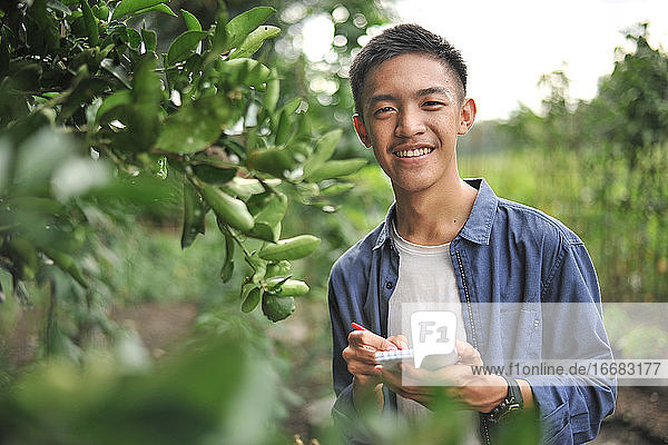 Happy of lächelnd junge asiatische Bauer männlich hält das Notebook auf grünen Garten