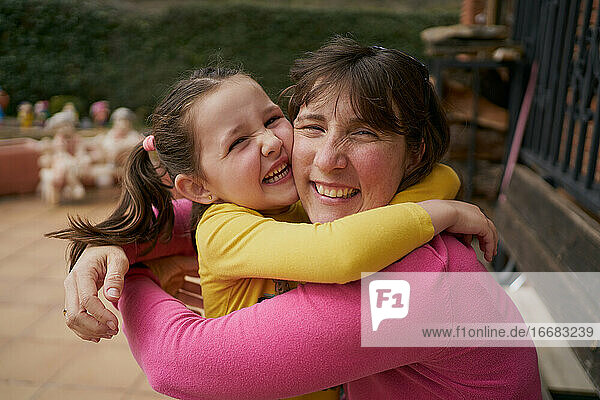 Seitenansicht einer fröhlichen Frau  die ihre Tochter umarmt und sich auf einer Bank ausruht