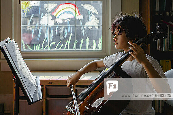 Ein konzentrierter Junge sitzt vor einem bemalten Fenster und übt Cello