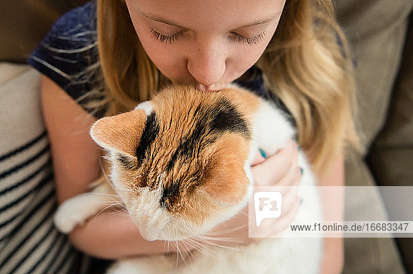 Close Up of Young Girl Kissing Calico Cat at Home