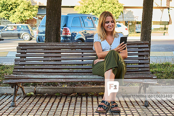 Junge Frau schaut auf ihr Telefon  während sie auf einer Bank sitzt