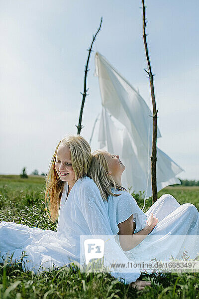 zwei blonde Mädchen sitzen im Sommer im Gras und lachen