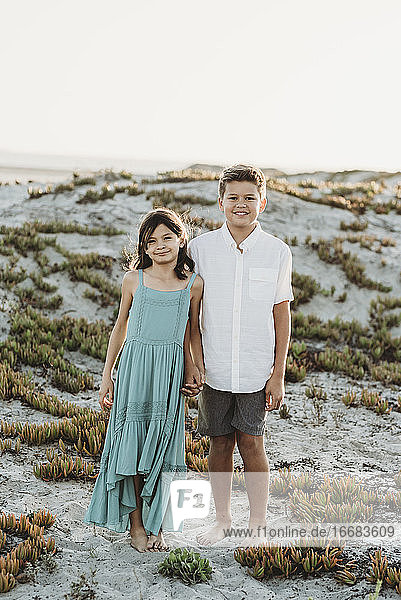 Glücklicher 12-jähriger Bruder und 8-jährige Schwester halten sich am Strand an den Händen