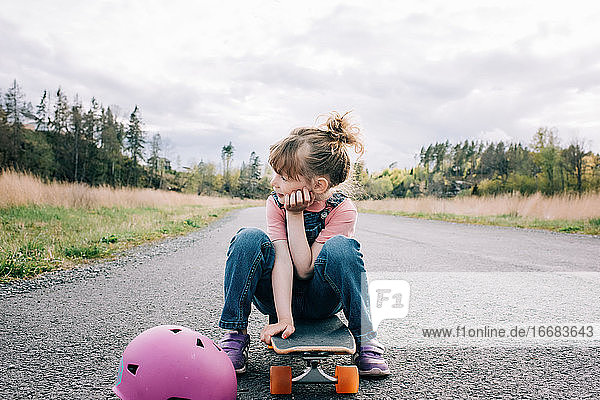 Porträt eines jungen Mädchens  das auf einem Skateboard sitzt und denkt